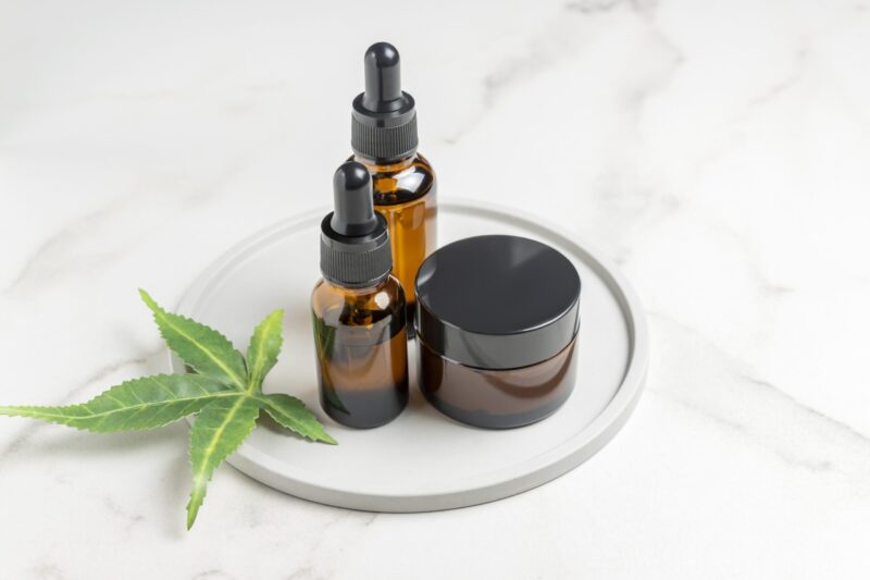 Three CBD product bottles arranged on a table next to a hemp leaf – natural recovery support for pain relief and muscle relaxation.