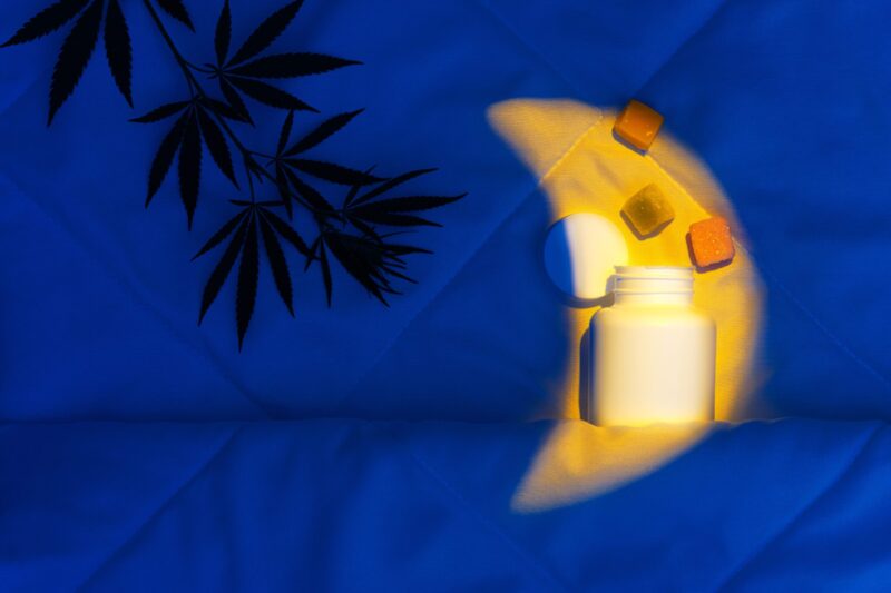 Open bottle of CBD gummies above it, tucked into soft sheets with a crescent moon-shaped light – sleep support for relaxation and rest.