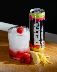 delta water can next to glass with ice and raspberry and lemons on table