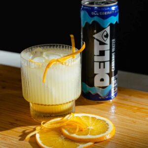 can of delta water on table next to glass of ice and lemon or orange slices
