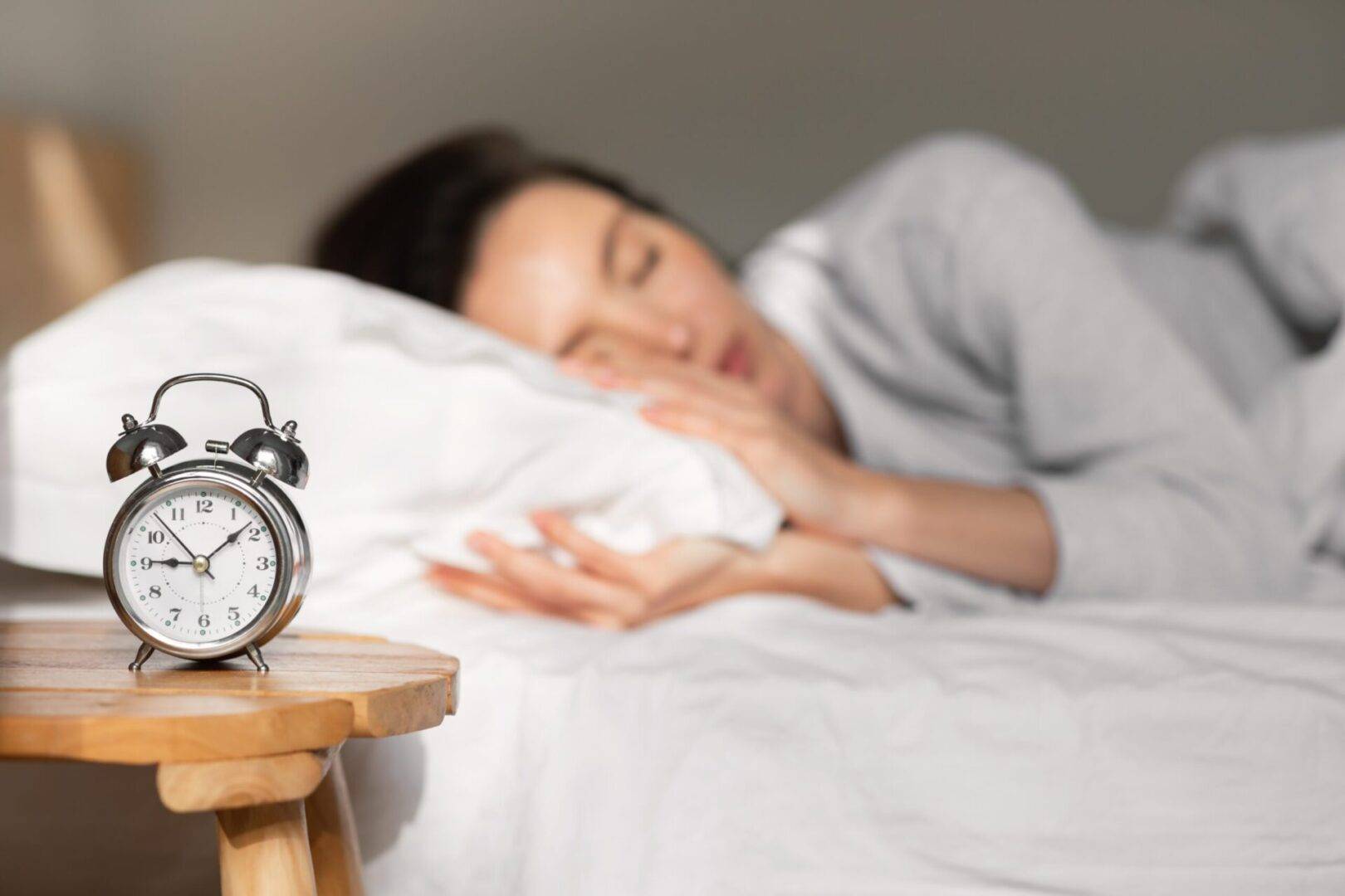 Woman peacefully sleeping in bed with an alarm clock in the foreground – CBD for better sleep and relaxation.
